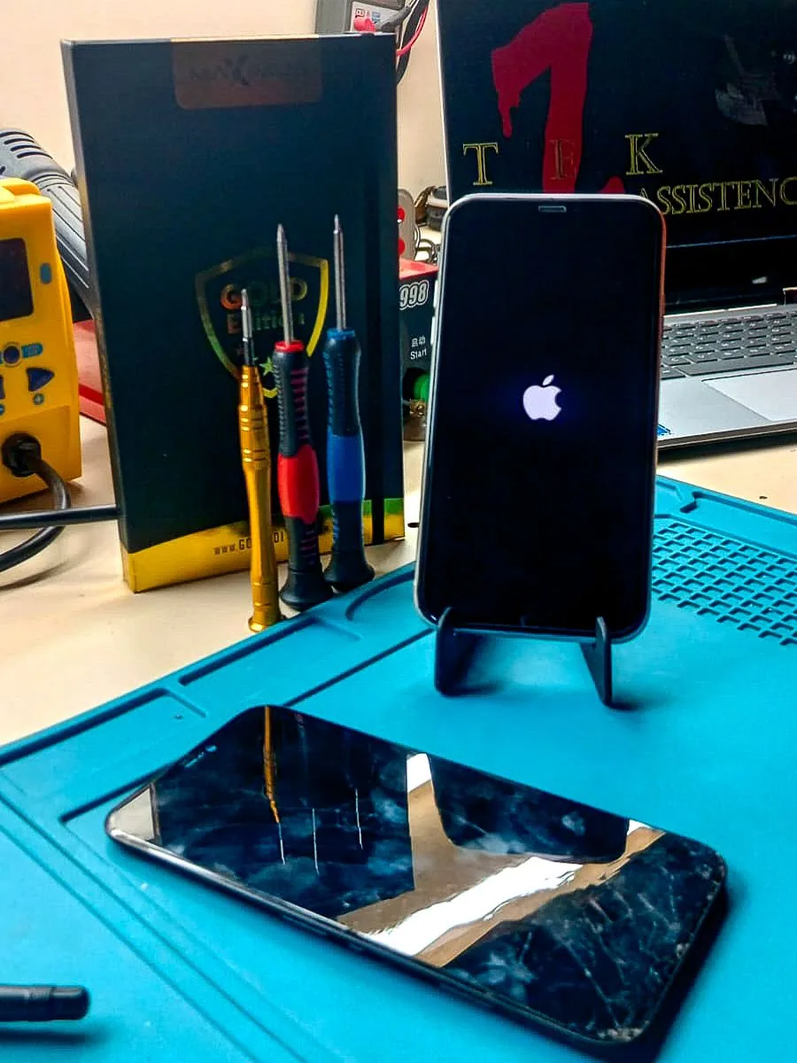 iPhone 11 funcionando após troca de tela, com tela antiga quebrada sobre a bancada