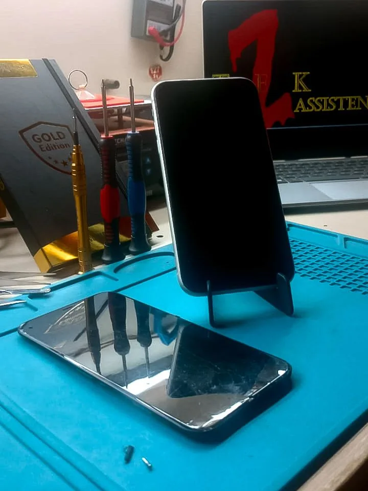 iPhone 11 após reparo, com a tela danificada refletindo as ferramentas da bancada