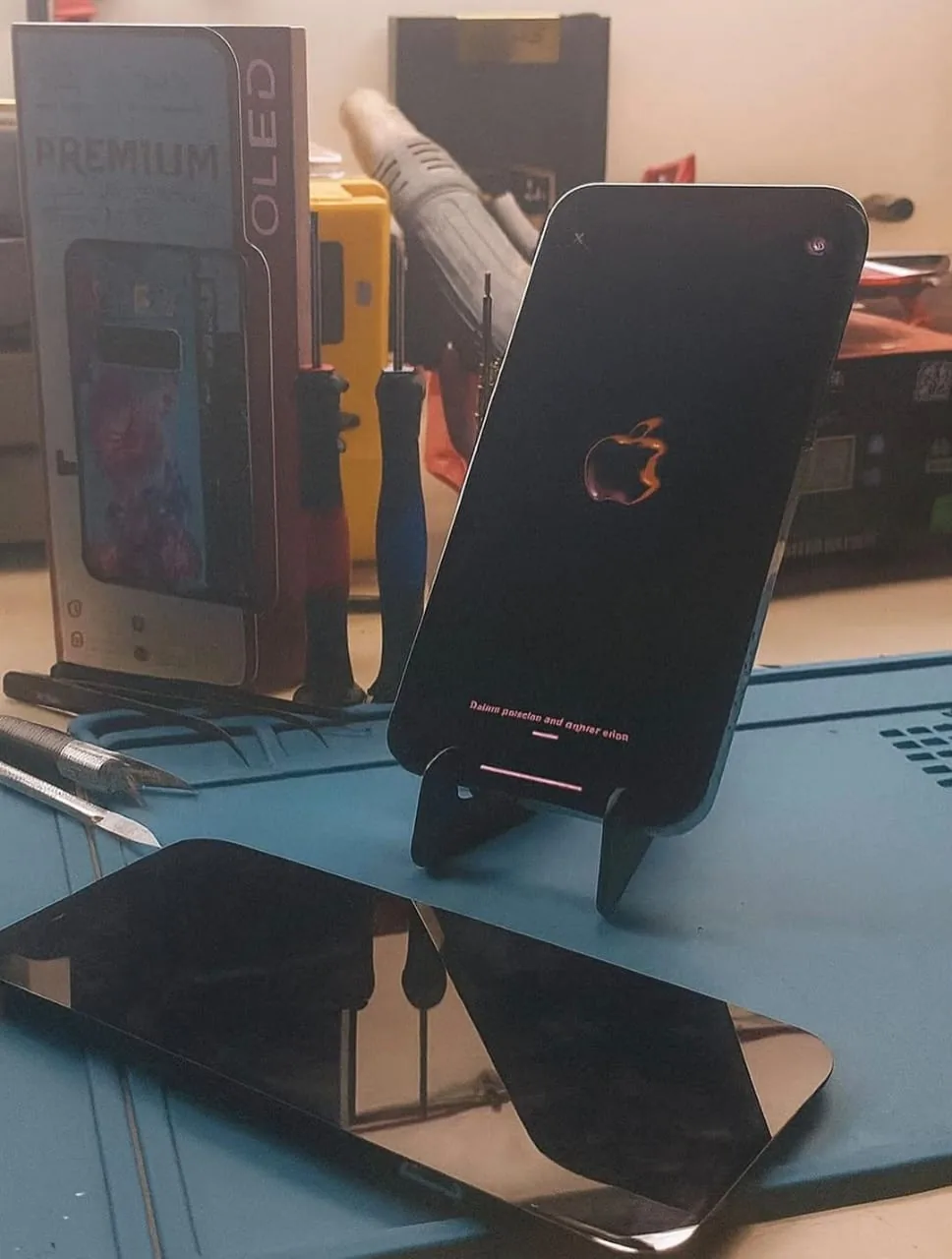 iPhone 13 Pro Max ligado após troca de tela, com tela antiga sobre a bancada