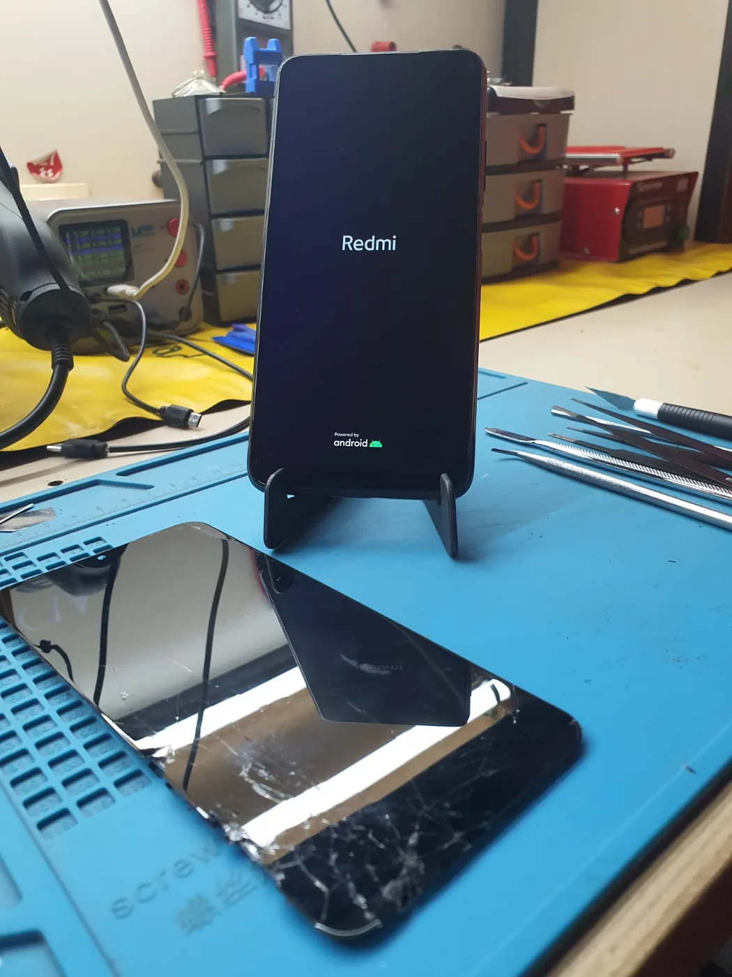 Xiaomi Redmi 9T funcionando após troca de tela e limpeza, com tela antiga quebrada na bancada